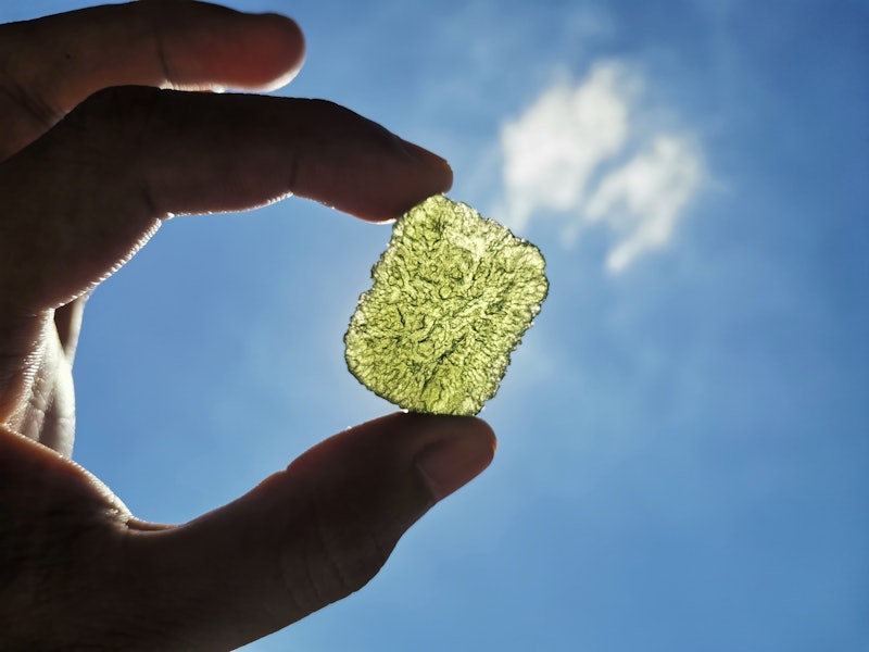 A piece of moldavite crystal against the sky. Experts explain how to use moldavite crystals and thei...