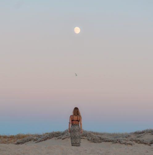 A woman sits on the beach watching the rising full moon. Here's your daily horoscope for november 19...