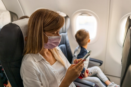 Pretty woman using a smartphone while sitting in an airplane with her child next to her.