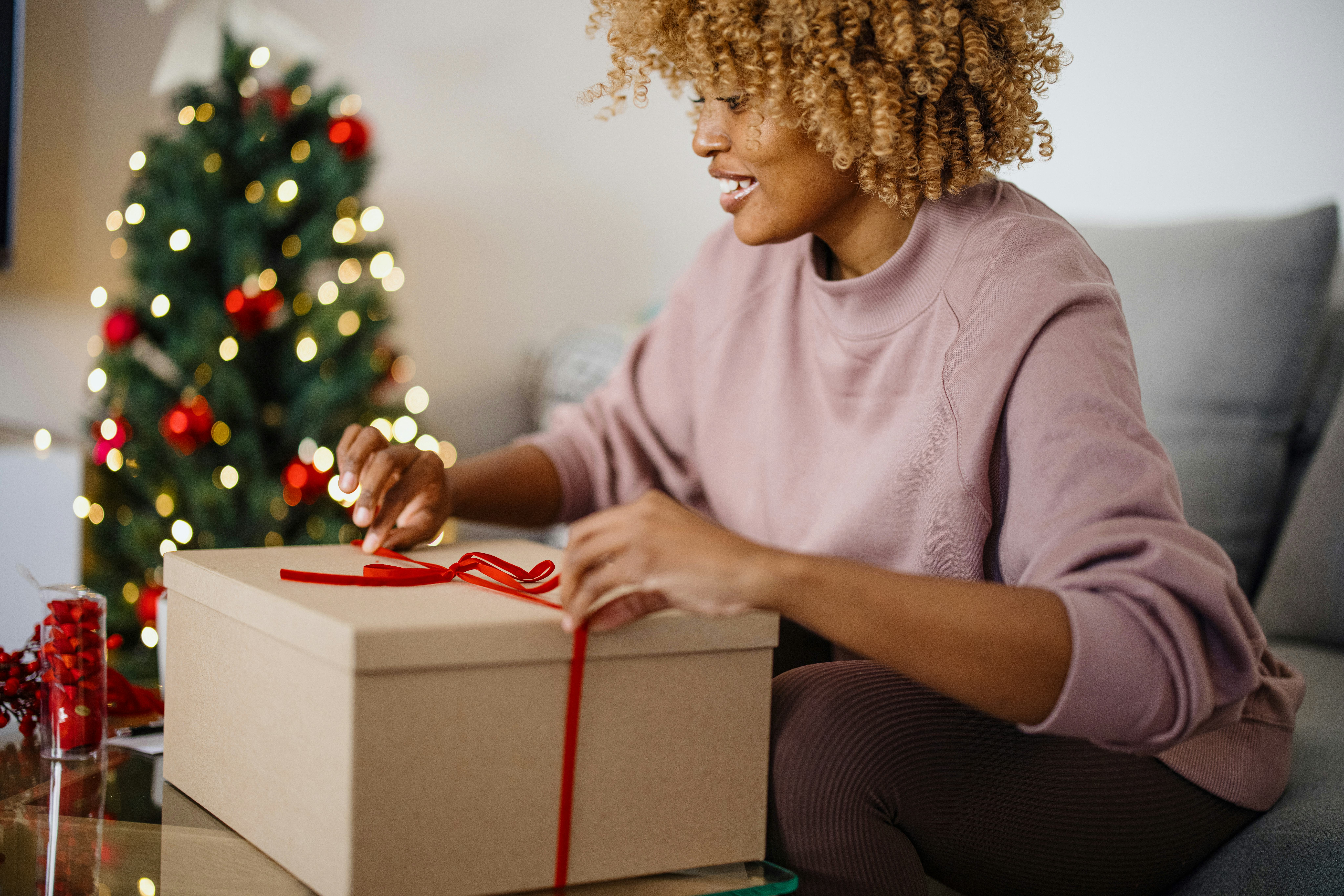 Woman wrapping Christmas presents in her home. Woman wrapping gift box in front of a Christmas tree