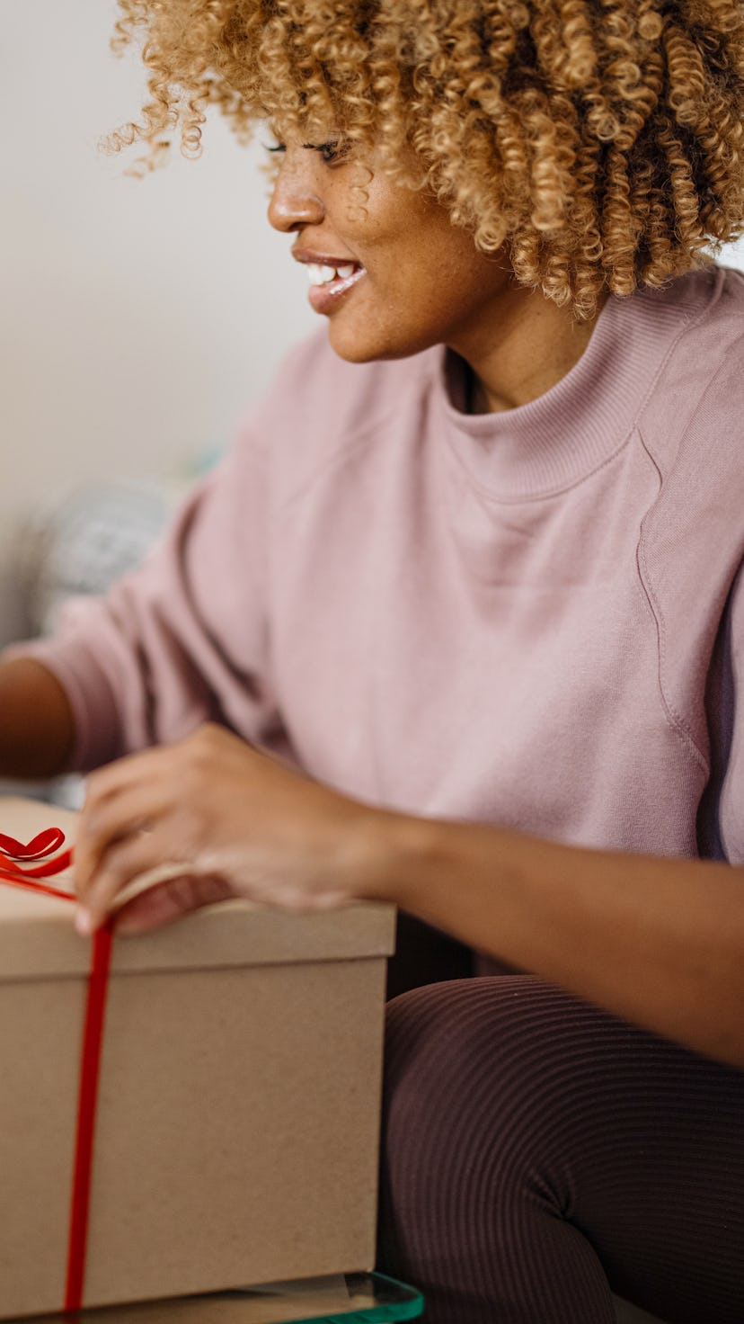 Woman wrapping Christmas presents in her home. Woman wrapping gift box in front of a Christmas tree