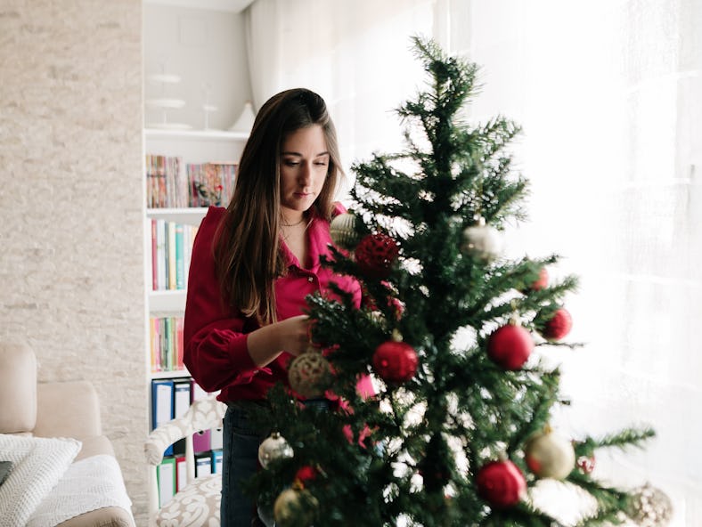 A woman decorating her home and Christmas tree with the 2021 holiday home decor trends.