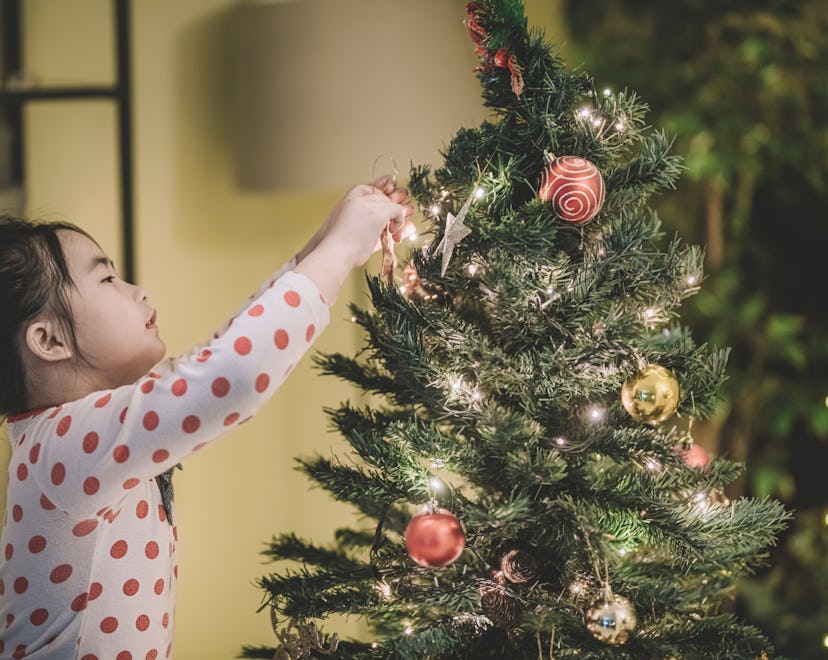 A child hanging decorations on a Christmas tree, up before Thanksgiving.