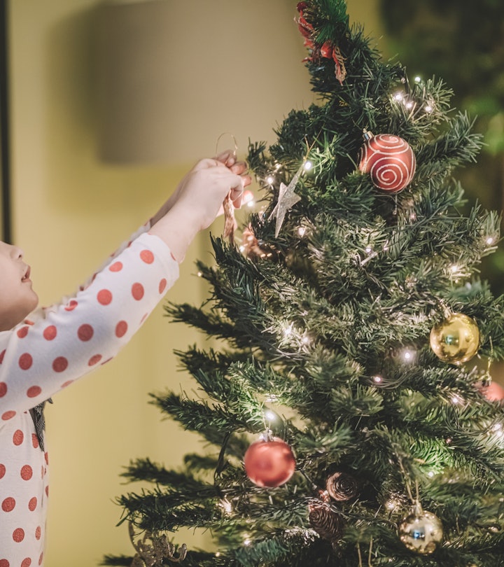 A child hanging decorations on a Christmas tree, up before Thanksgiving.