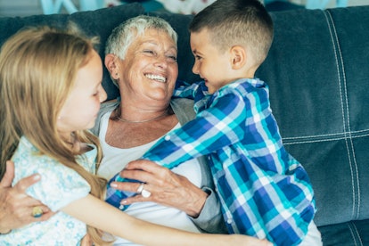 Grandmother embracing her cute grandson and granddaughter on the sofa at home.