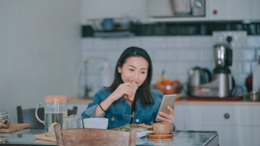 A young woman enjoys her breakfast at home while reading the response to a text she just sent.