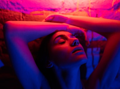 Young woman posing under the bright neon lights, thinking about the spiritual meaning of the Decembe...