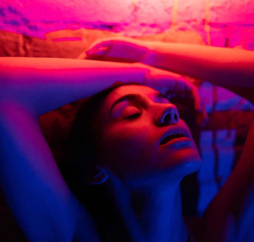 Young woman posing under the bright neon lights, thinking about the spiritual meaning of the Decembe...