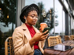 A young woman drinks a cup of coffee while texting a crush from her hometown.