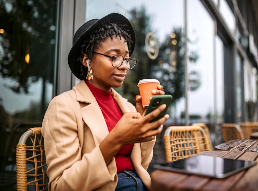 A young woman drinks a cup of coffee while texting a crush from her hometown.