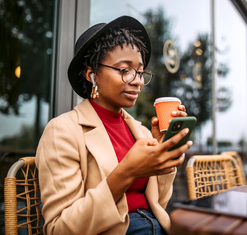 A young woman drinks a cup of coffee while texting a crush from her hometown.
