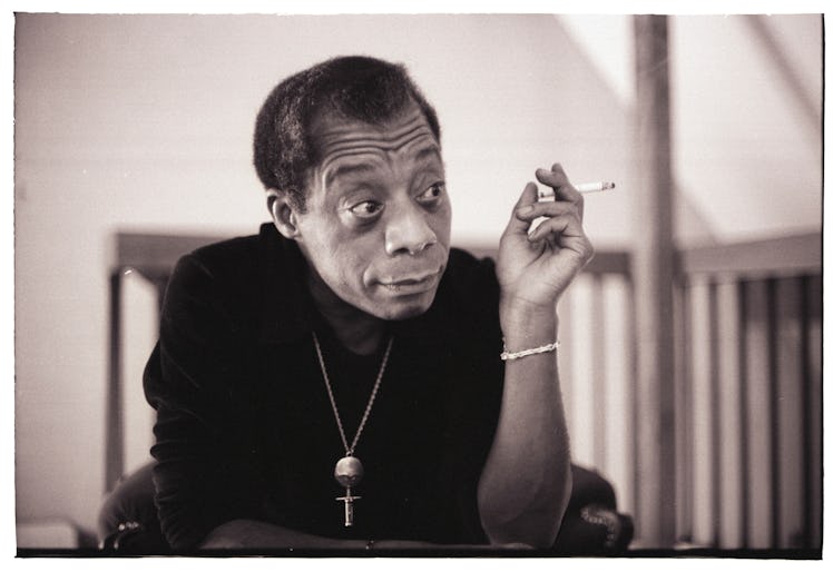 American writer James Baldwin in a black shirt smoking a cigarette