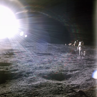 A brilliant sun shines above the Apollo 12 base on the Moon's surface. One of the astronauts walks a...