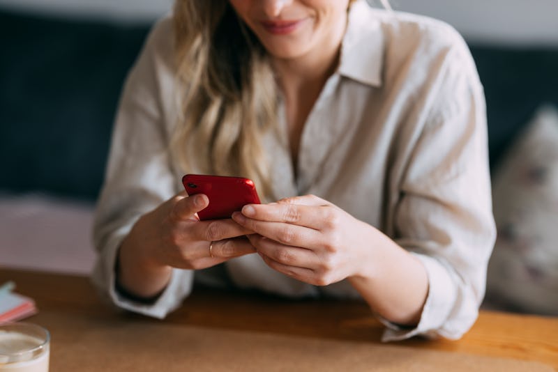 An anonymous businesswoman sitting at home office desk and typing text message on her smartphone in ...