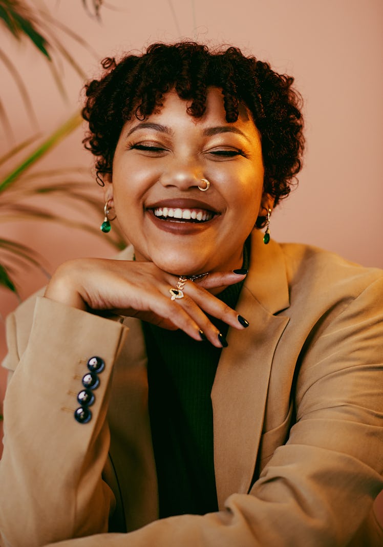 Young woman laughing while wearing beige coat, thinking about how January 2022 will be the best mont...