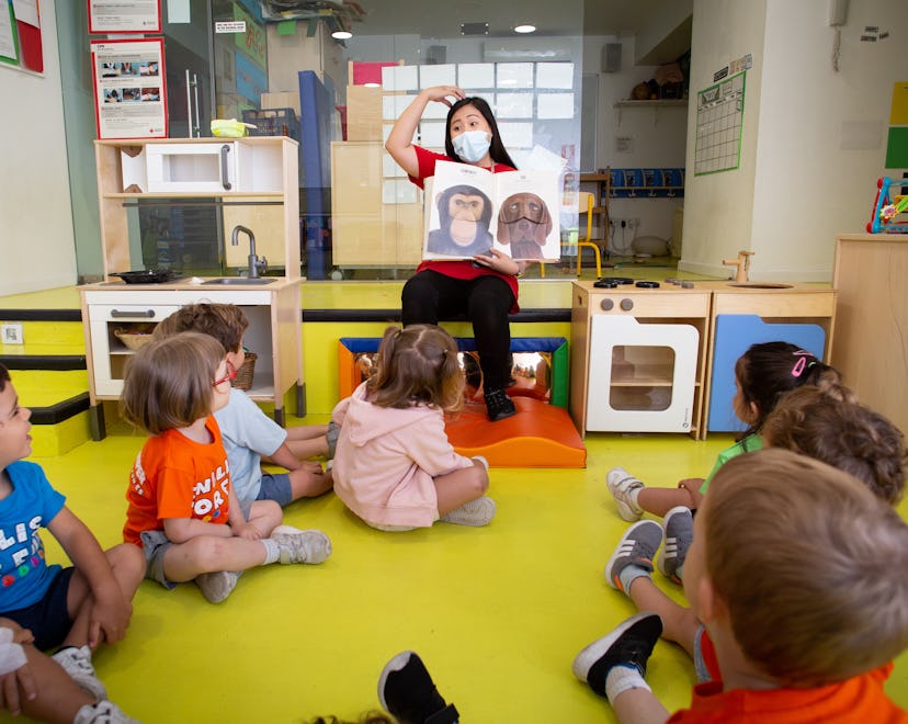 A teachers wearing a protective face mask reads a book to children while making dramatic faces on Ju...