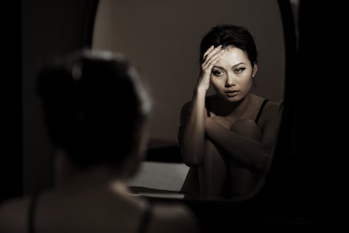 Sad crying woman sitting at the mirror in dark room