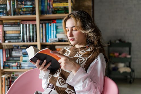 Stylish young girl is sitting in her room and reading book