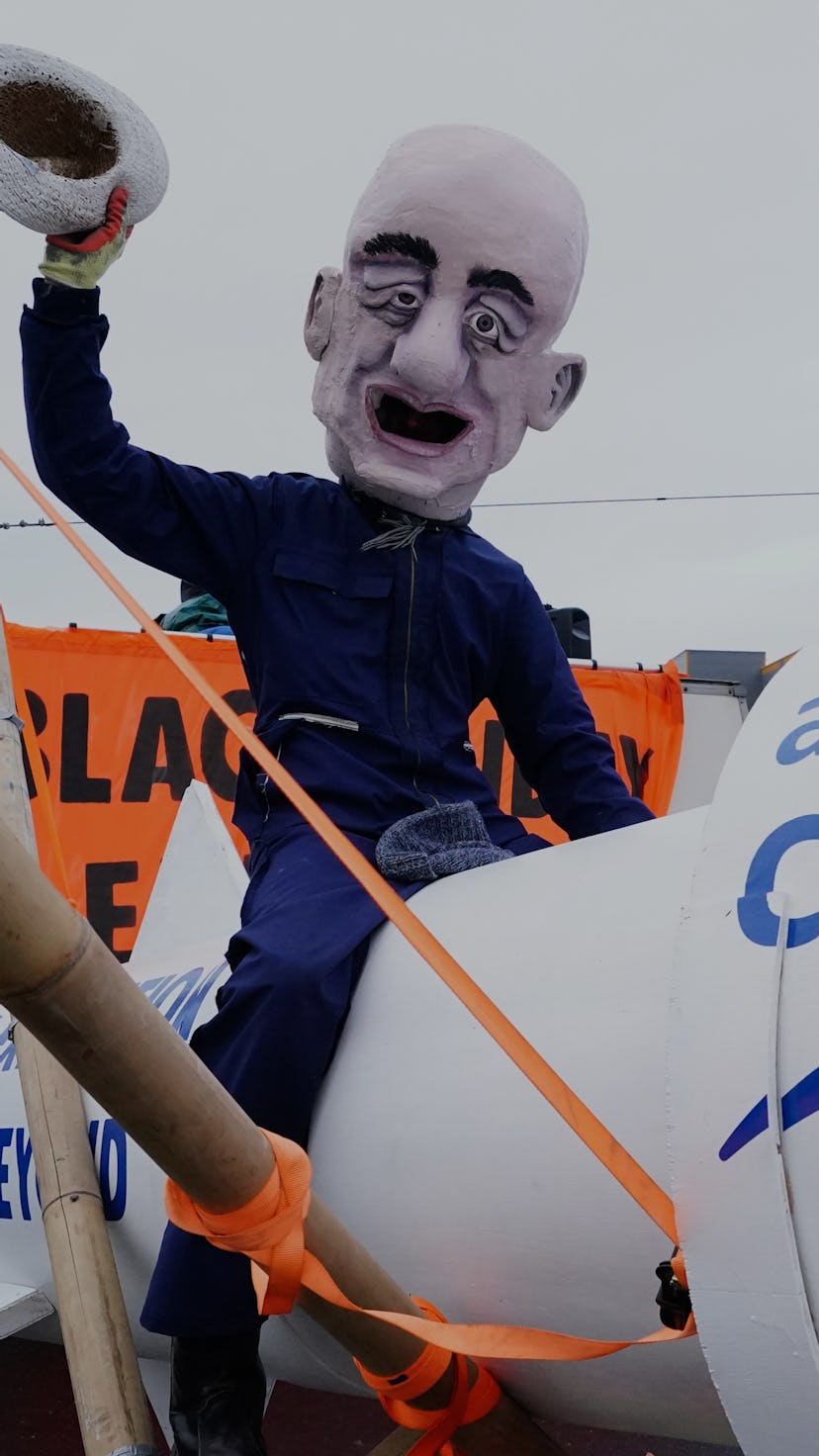 An activist from Extinction Rebellion, wearing a giant Jeff Bezos head, blocks the entrance to the A...
