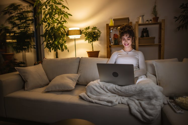 Photo of a young woman using her laptop on the sofa looking for the best Cyber Monday deals to post ...