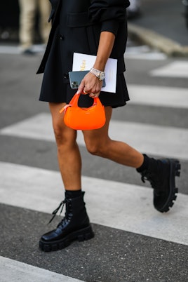 A guest wears a black coat, a black dress, a neon orange leather small Coperni handbag, black shiny ...