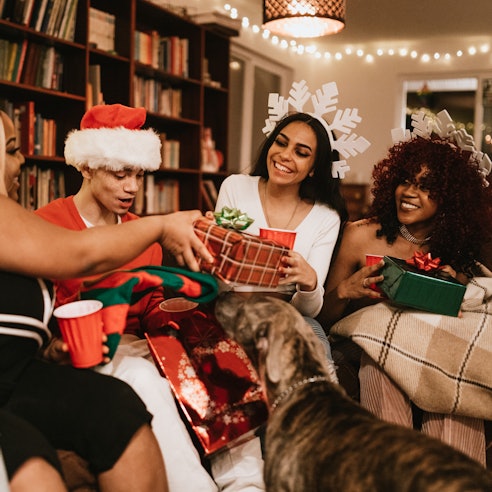 A group of young adult friends gather at a home for Christmas celebration over the holiday, dressed ...