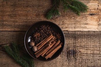 Christmas natural spices in ceramic bowl, baking ingredients on rustic wooden table viewed from abov...