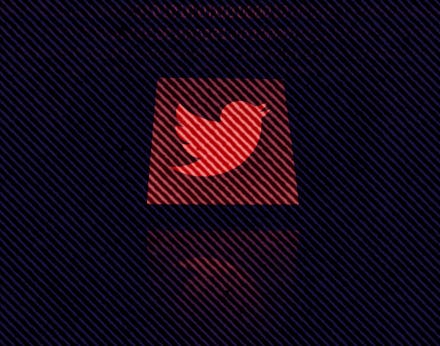 Twitter logo displayed on a phone screen is seen with binary code displayed on a laptop screen in th...