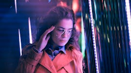 Young woman standing in neon light, thinking about how the December 2021 new moon solar eclipse will...