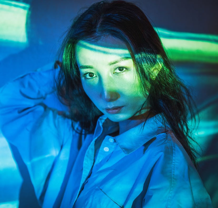 Young woman standing in blue neon light, thinking about how the December 2021 new moon solar eclipse...
