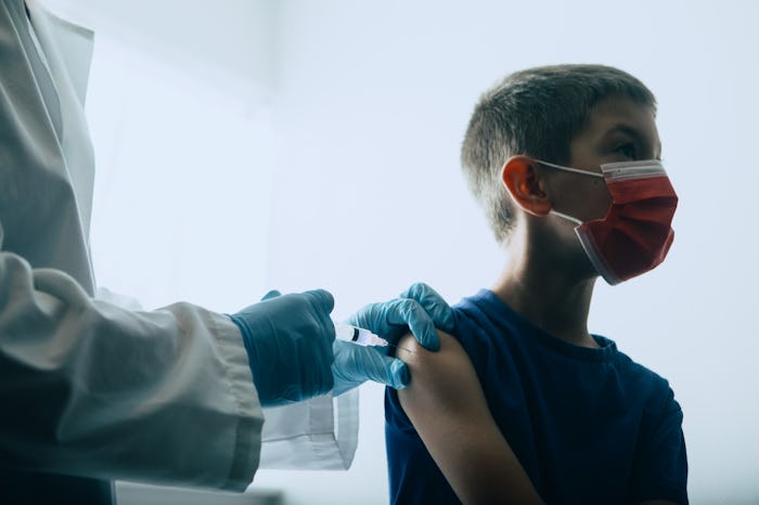 A Caucasian boy receives a vaccine, possibly for COVID-19 Coronavirus, administered by a female Dr.