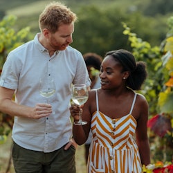 Diverse lovely couple toasting while walking through vineyard