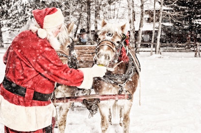 Outdoor Snowing Scene.  Santa in his red suit feeding a team of horses a green apple.  There is a co...