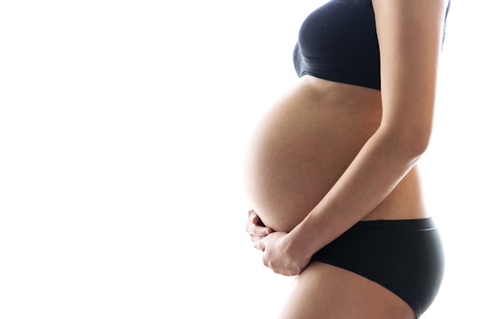 Image of a pregnant person standing and cradling their pregnant belly. 