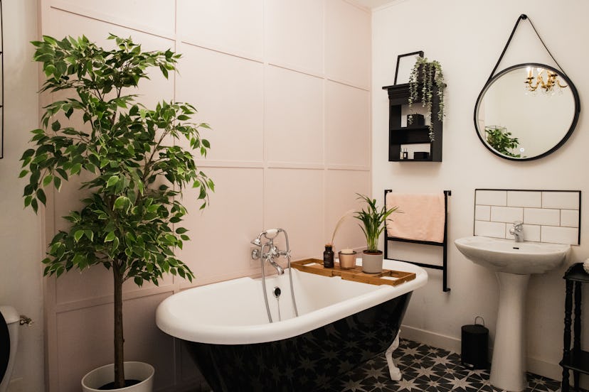 A shot of a modern bathroom interior with houseplants and a candle on the bathtub.