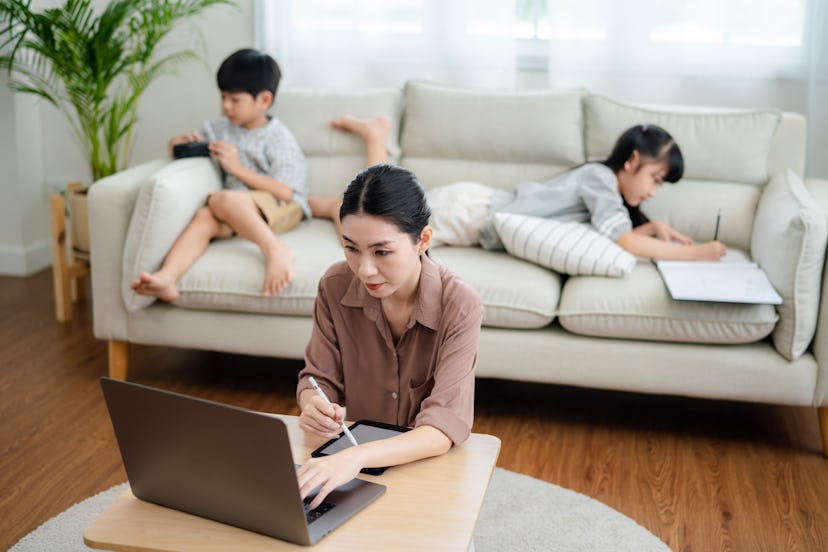 Asian mother working with laptop while her son and daughter are playing in the living room.