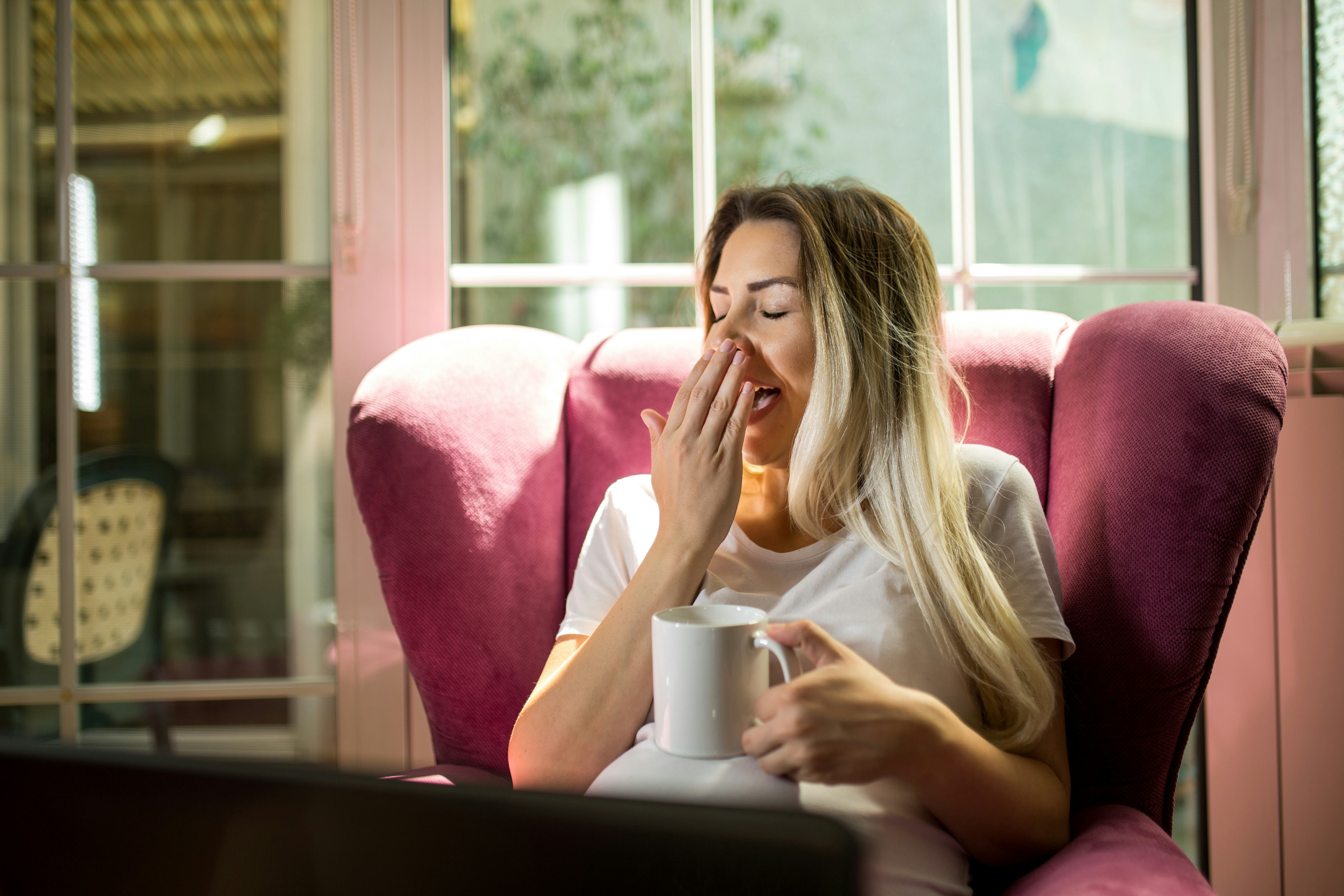 Pregnant young woman yawning and drinking coffee