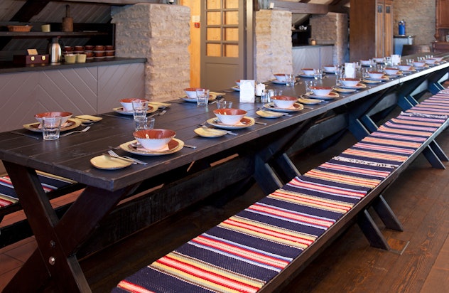 Image of a long rectangular table, set for a meal, with long sitting benches on either side. 