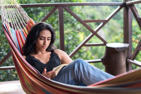 casually dressed average age 25-year-old Latina woman is in her vacation cabin sitting in her hammoc...