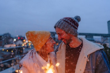 Young couple with sparklers on a rooftop terrace, thinking about how winter 2021 will be the most ro...