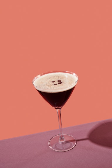 an espresso martini served in a cocktail glass, on a table set with a maroon tablecloth, against a c...