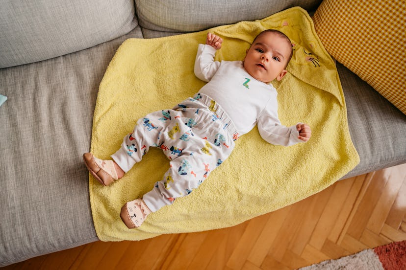 A shot of a cute baby lying down on the sofa in the living room and looking at camera.