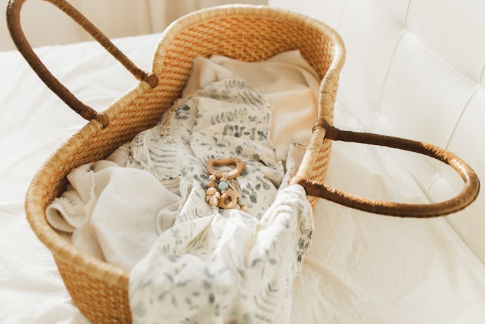 Baby clothes, muslin diaper and toy in moses basket. Preparation for the appearance of a child. Expe...