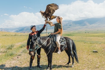 Young female tourist with long hair sitting on the horse holding Eagle and the hunter in traditional...