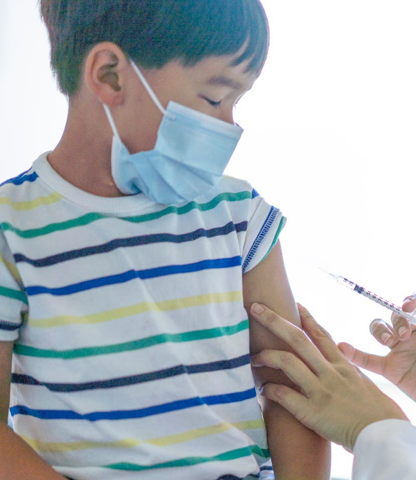 A sweet little boy of Asian decent sits up on an exam table as he looks down at his arm nervously.  ...