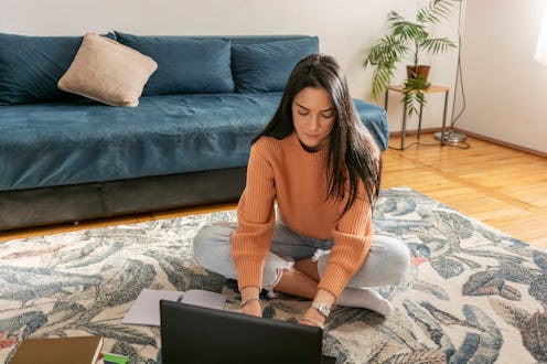 Young woman sitting on carpet in living room and looking at laptop