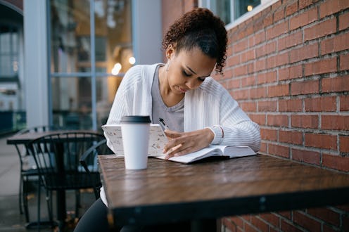 A mixed race women reads a large Bible / textbook while seated at table outdoors. Could also be a u...