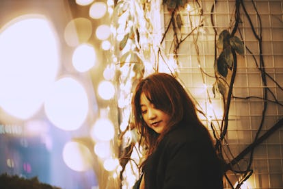 Young woman basking in bright string lights, waiting to hear her December 20, 2021 weekly horoscope.