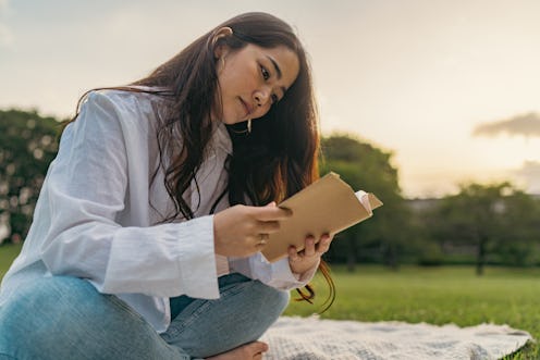 A beautiful young woman is enjoying reading a book in nature.