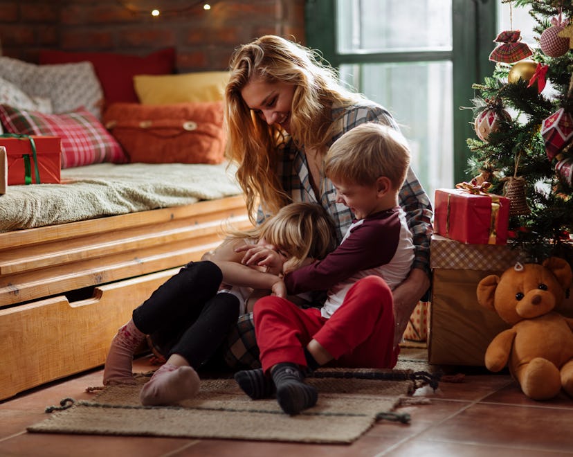 Little brother and sister sitting on their living room floor with their mom on Christmas morning